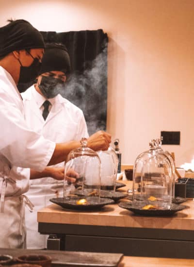 Chefs preparing the final beef dish presented in a glass smoking cloche dome at Rebel Omakase in Laguna Beach